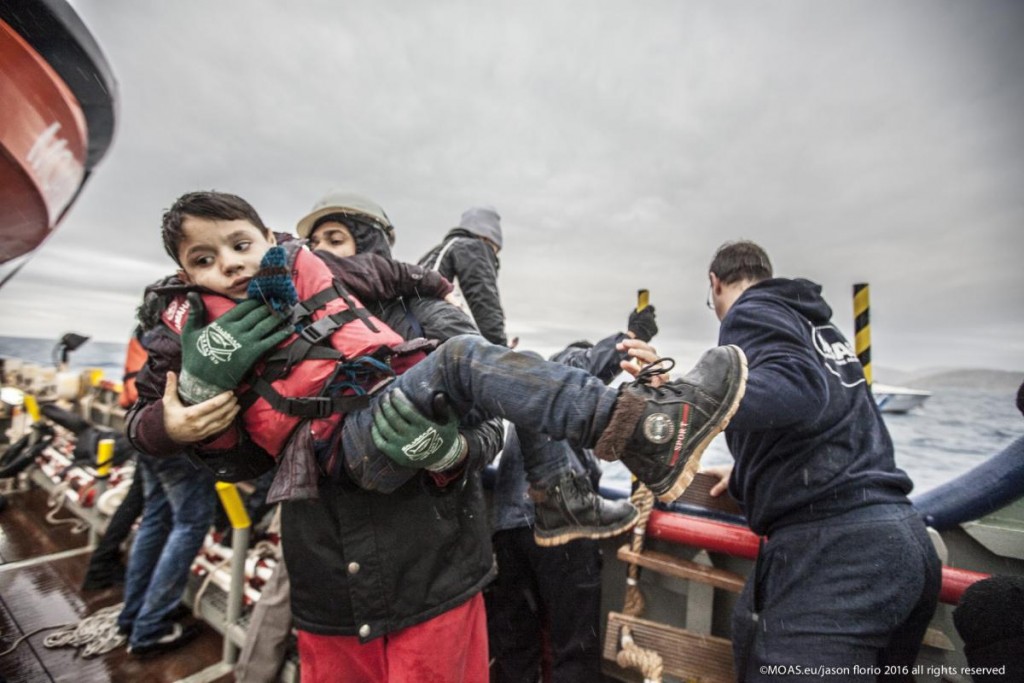 A young Syrian child is lifted to safety from an overloaded open boat carrying 55 migrants. Photo: MOAS