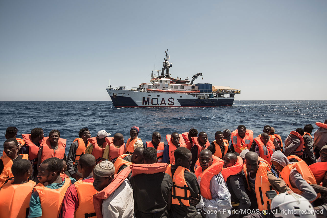 migrants-in-unstable-boat-in-Central-Mediterranean-waiting-to-be-rescued-my-phoenix-in-the-background-copyright-Jason-Florio_MOAS-2016-6585