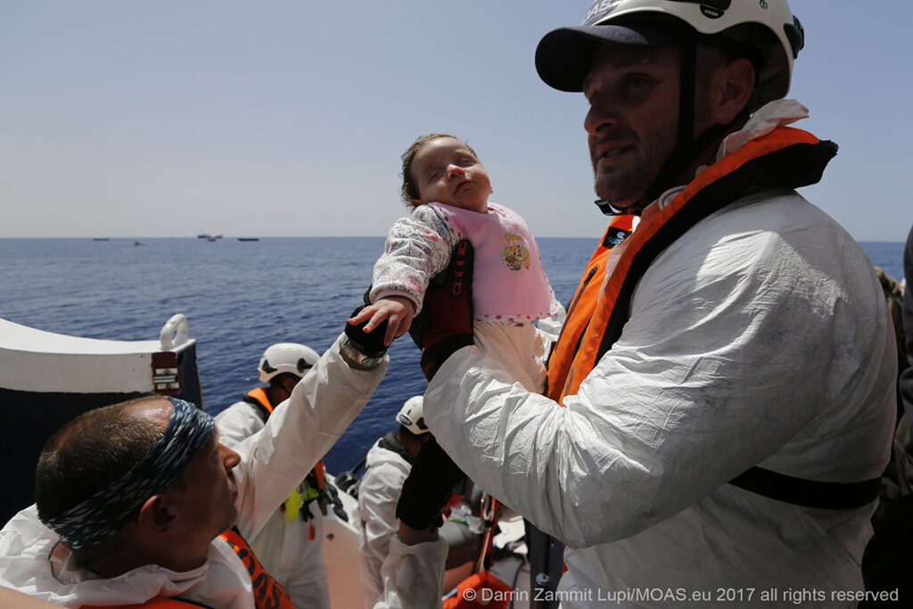An infant is brought on board the MOAS rescue ship Phoenix, after being rescued along with her mother and father and numerous other refugees and migrants.