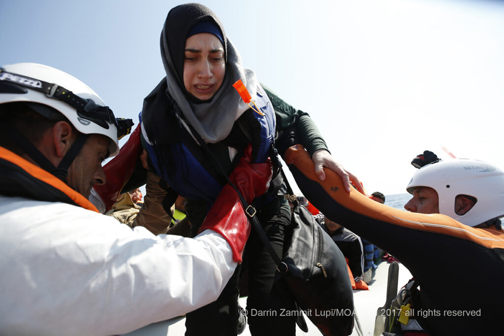 Scared and afraid, a young woman is helped onto the rescue RHIB by MOAS crew after spending hours at sea in a rubber boat with hundreds of people on board.