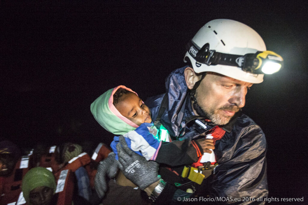Igor, a MOAS crew member, carefully helps a young child off of a rickety boat and onto the safety of the Phoenix.